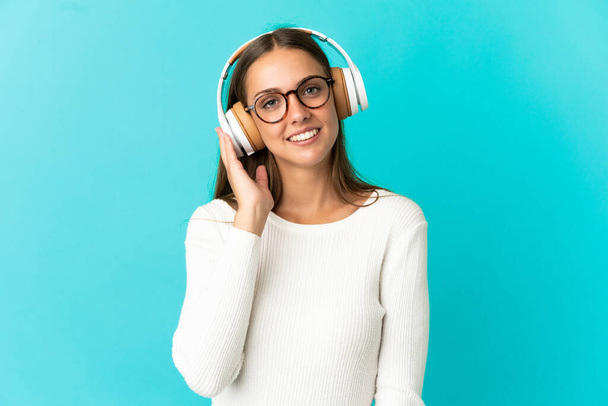 Young woman over isolated blue background listening music - Foto, imagen