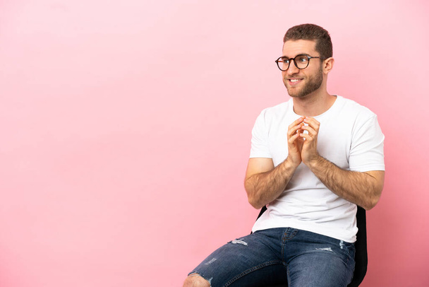 Young man sitting on a chair over isolated pink background scheming something - Photo, Image