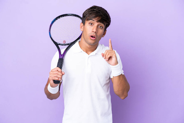 Handsome young tennis player man isolated on ocher background intending to realizes the solution while lifting a finger up - Photo, Image