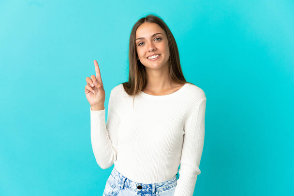 Junge Frau auf isoliertem blauem Hintergrund zeigt und hebt einen Finger im Zeichen des Besten - Foto, Bild