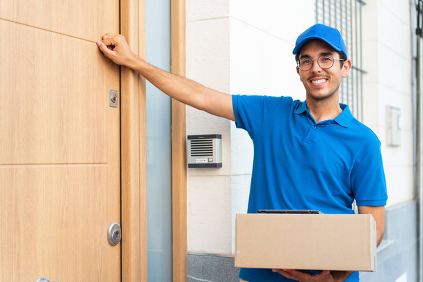 Young delivery man at outdoors holding boxes and knocking on the door - Фото, изображение