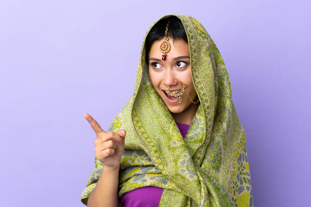 指を持ち上げながら解決策を実現しようと紫色の背景に隔離されたインドの女性 - 写真・画像