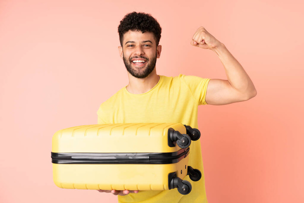 Young Moroccan man isolated on pink background in vacation with travel suitcase - Фото, зображення