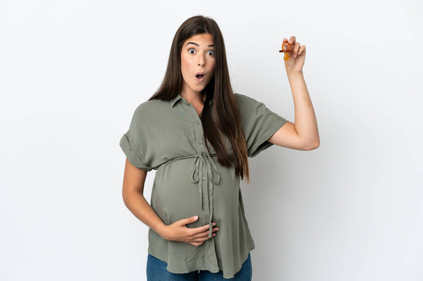 Giovane donna brasiliana isolata su sfondo bianco incinta e con in mano un ciuccio con espressione sorpresa - Foto, immagini