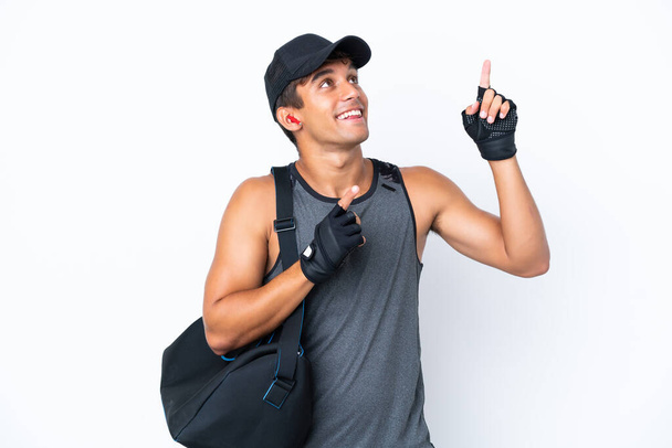 Молодой кавказский спортсмен со спортивной сумкой на белом фоне указывает указательным пальцем отличная идея - Фото, изображение
