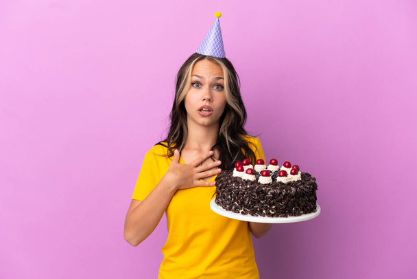 Adolescente russe fille tenant gâteau d'anniversaire isolé sur fond violet surpris et choqué tout en regardant à droite - Photo, image
