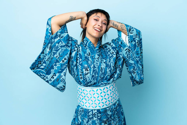 Νεαρή γυναίκα που φοράει κιμονό πάνω από απομονωμένο μπλε φόντο γελώντας - Φωτογραφία, εικόνα