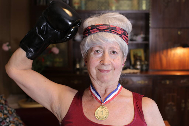 Nahaufnahme Porträt einer reifen Frau im Boxerkostüm mit Goldmedaille zu Hause, Konzept der Halloween-Feier - Foto, Bild
