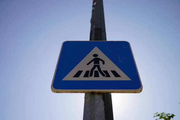 A pedestrian crossing road sign on the metal post in the blue sky background - Foto, imagen