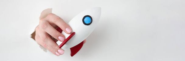 Female hand holds rocket through hole in white paper - Фото, зображення