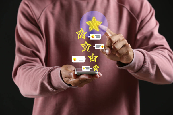Young man giving rating to new mobile application on dark background - Photo, image