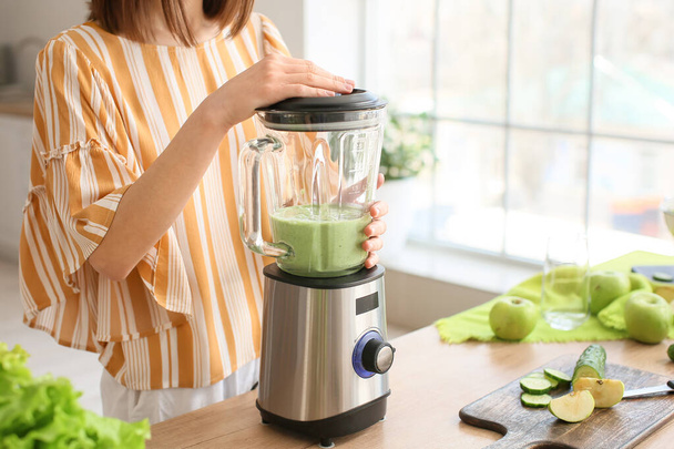 Young woman preparing healthy green smoothie in kitchen - Foto, imagen