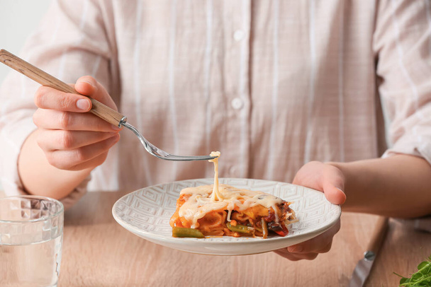 Woman eating tasty vegetable lasagna at table, closeup - 写真・画像