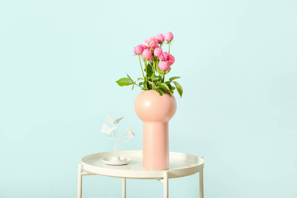 Vase with beautiful peony roses on table against color wall - 写真・画像