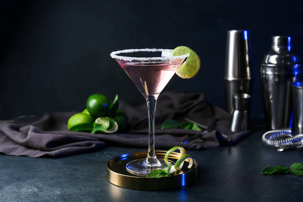 Glass of tasty cosmopolitan cocktail, shakers and limes on dark background - Photo, Image