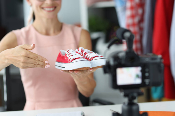 Woman salesman consultant shows to camera red sports shoes - Fotoğraf, Görsel