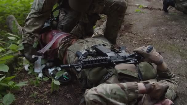 Médecin de combat prenant la trousse de premiers soins, appliquant un bandage sur la jambe blessée - Séquence, vidéo