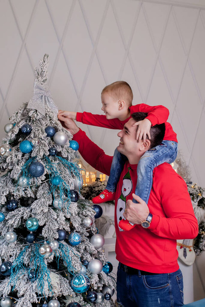Happy Father and son enjoying decorating Christmas tree with Christmas balls and light garland preparing for celebrating winter holidays: Merry Christmas Eve and Happy New Year 2021. Family concept. - Zdjęcie, obraz