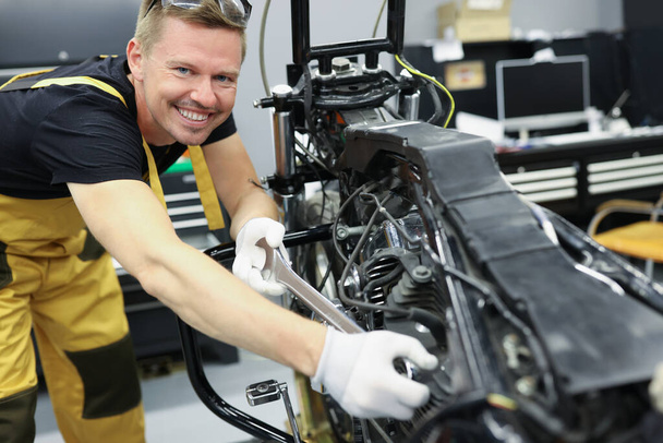 Schlosser-Mechaniker mit Schraubenschlüssel steht neben Motorradmotor - Foto, Bild
