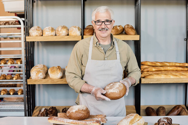 Šťastný starý pekař v pracovním oděvu při pohledu na vás na pracovišti - Fotografie, Obrázek