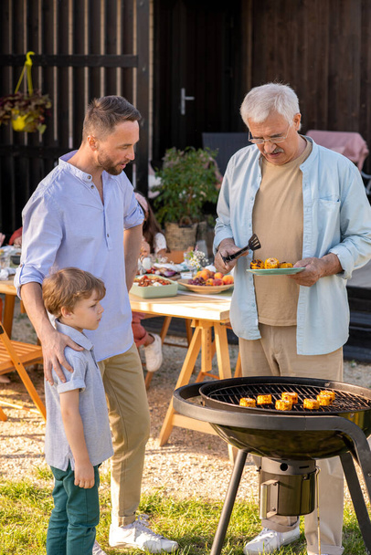 Mature man, his son and grandson making grilled corn for family dinner - Foto, imagen