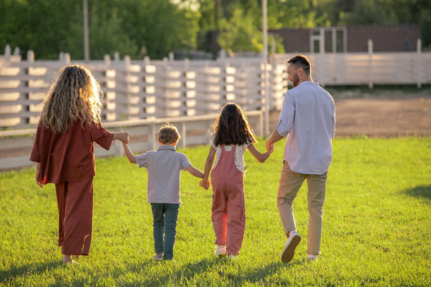 両親と2人の子供が田舎の緑の芝生を歩いている - 写真・画像