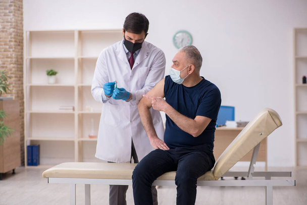 Paciente do sexo masculino idoso visitando jovem médico do sexo masculino em conce vacinação - Foto, Imagem