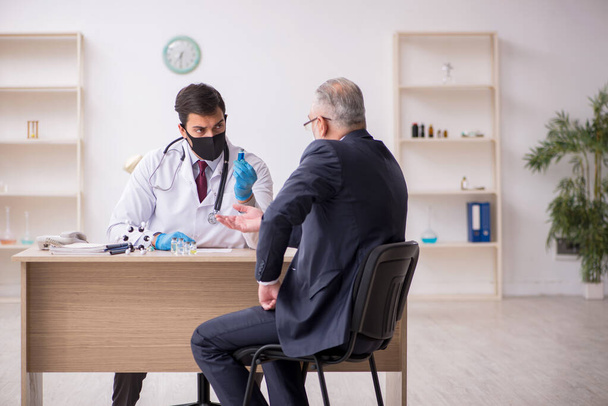 Old businessman visiting young male doctor in vaccination concep - Photo, Image