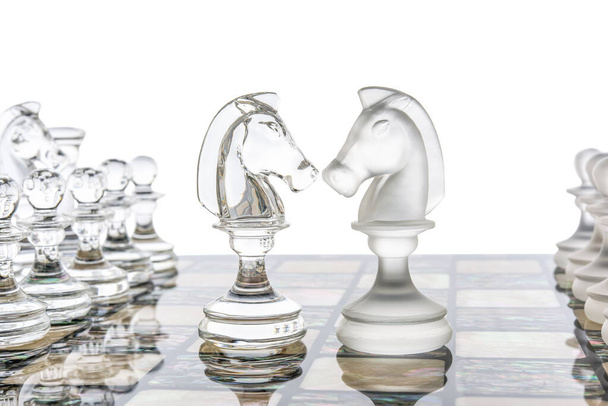 Différentes pièces en verre transparentes figurines d'échecs debout sur un plateau de perles en blanc. Ensemble de formes brillantes et mates. concept de jeu de confrontation. Gros plan doux. - Photo, image