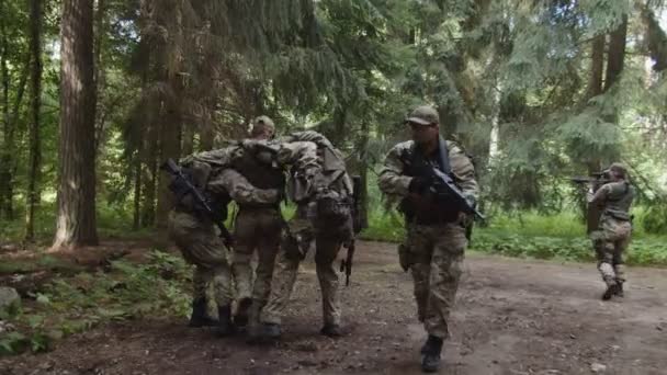 Military squad covering injured soldier to evacuation point in forest - Footage, Video