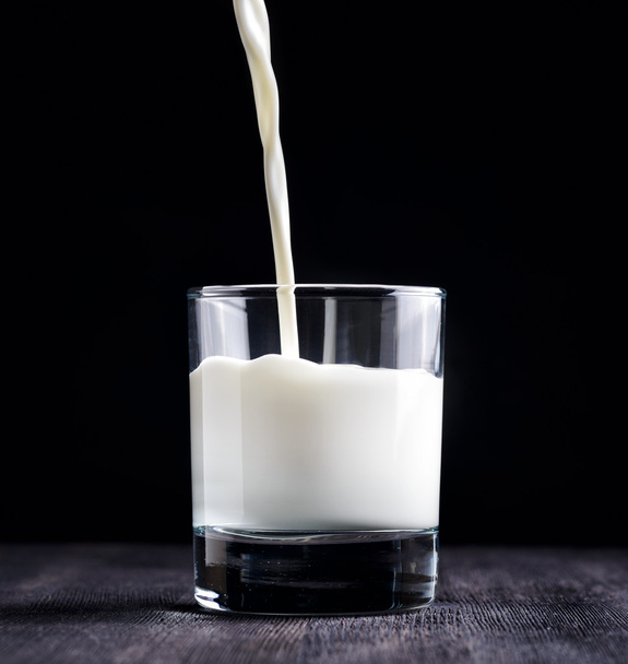 Milk pouring into a glass on black board - Photo, image