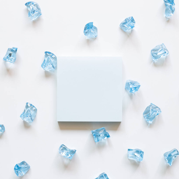 Bloc de notas en blanco con cubitos de hielo azul sobre fondo blanco. vista superior, espacio de copia - Foto, Imagen