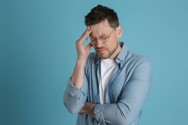 Man lijdt aan vreselijke migraine op lichtblauwe achtergrond - Foto, afbeelding