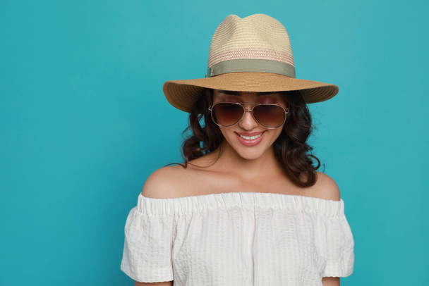 Beautiful young woman with straw hat and stylish sunglasses on light blue background - Zdjęcie, obraz