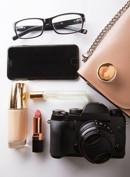 Flat lay of beige leather woman bag with cosmetics, accessories, camera and smartphone on white background. Beauty and fashion concept. - Φωτογραφία, εικόνα