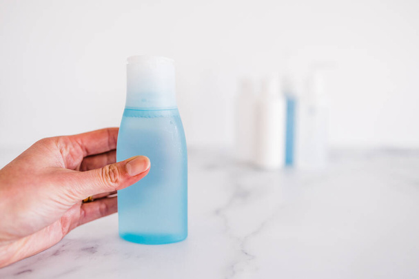 niska toksykologia i nietoksyczne naturalne produkty kosmetyczne konceptualny obraz, ręcznie wybierając niebieską butelkę balsamu na pierwszym planie, który wyróżnia się z grupy innych butelek   - Zdjęcie, obraz