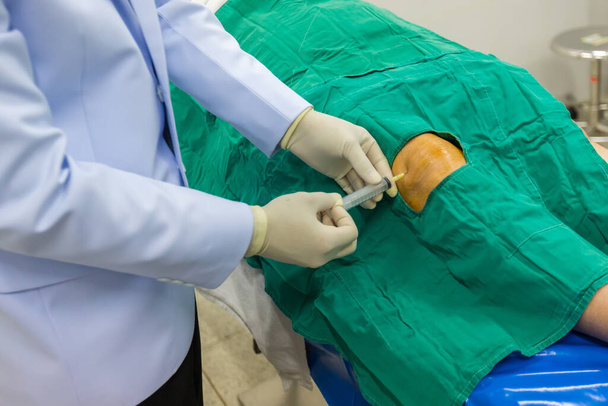 Doktor beyaz önlük giyer, hastanın dizine anestezi enjekte eder ve ameliyata hazırlanır.. - Fotoğraf, Görsel