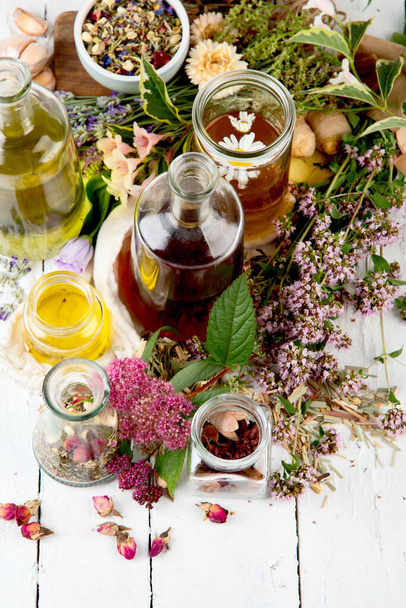 Various glass bottles with alternative medicine made of herbs and flowers on white wooden board. Copy space, top view, flat lay - Foto, afbeelding