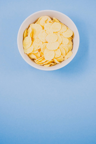 A bowl of cornflakes isolated on a blue background with free space for text - 写真・画像