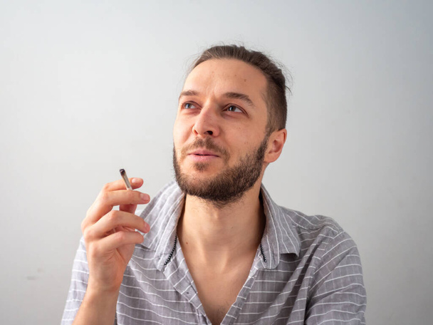 グレーシャツの白人男性がコロンビアのメデリンの白い部屋でタバコを吸う - 写真・画像