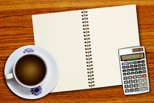 白いコーヒーのカップと木製のテーブルの背景に空白のページのノート上の電卓 - 写真・画像