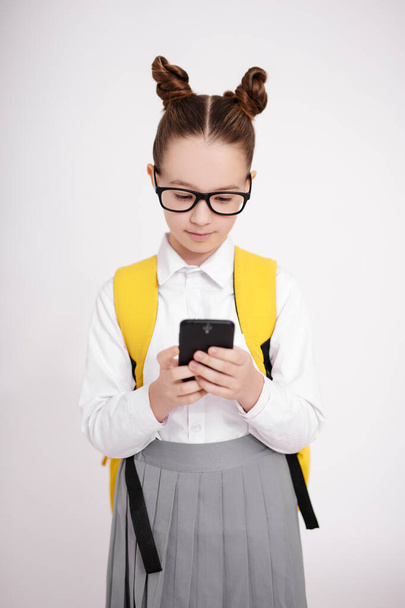 eğitim, sosyal medya ve internet bağımlılığı konsepti - okul üniformalı şirin bir kızın portresi ve beyaz arka plan üzerinde akıllı telefon kullanarak gözlük - Fotoğraf, Görsel
