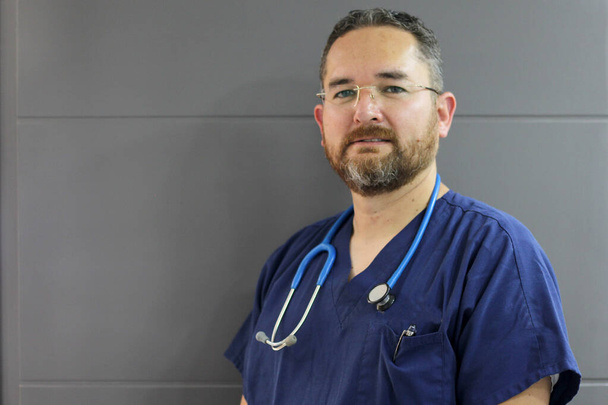 Professional mature medical doctor man, light eyes, beard with stethoscope and blue gallantdale, ready to work - 写真・画像