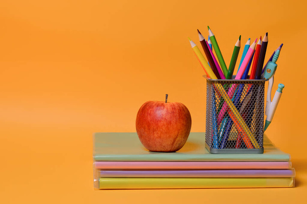 School supplies: notebooks, books, colored pencils, an apple on an orange background. Back to school. Copy space. - Фото, зображення