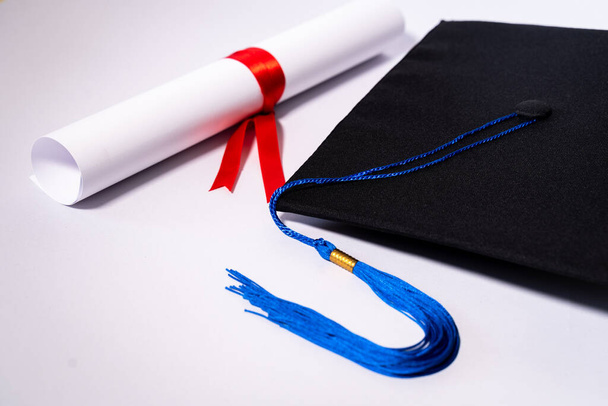 Stock photo of a graduation cap mortar board and diploma certificate isolated on white background with negative copy space to add text. Graduation hat with diploma on table against white background - Photo, Image