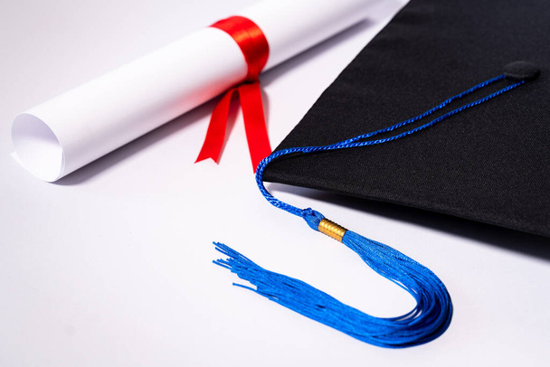 Stock photo of a graduation cap mortar board and diploma certificate isolated on white background with negative copy space to add text. Graduation hat with diploma on table against white background - Photo, Image