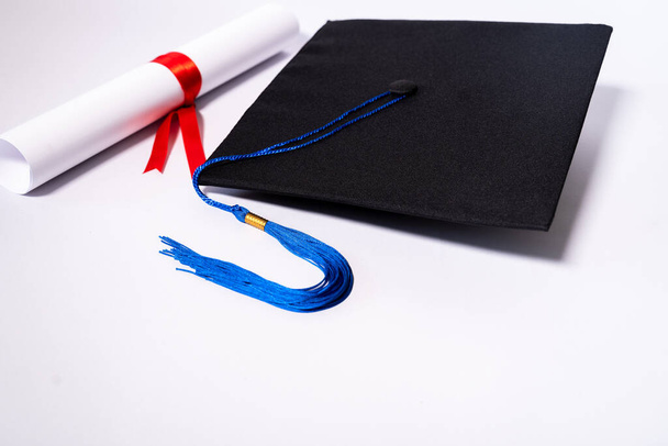 Stock photo of a graduation cap mortar board and diploma certificate isolated on white background with negative copy space to add text. Graduation hat with diploma on table against white background - Foto, imagen