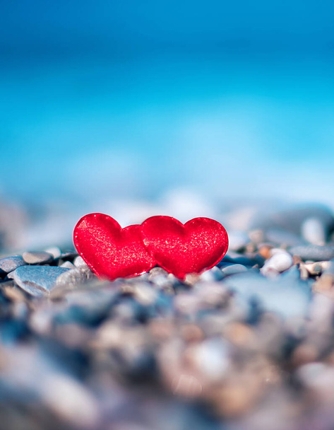dos corazones rojos sobre piedras sobre un fondo borroso en la orilla del mar. Símbolo de amor - Foto, imagen