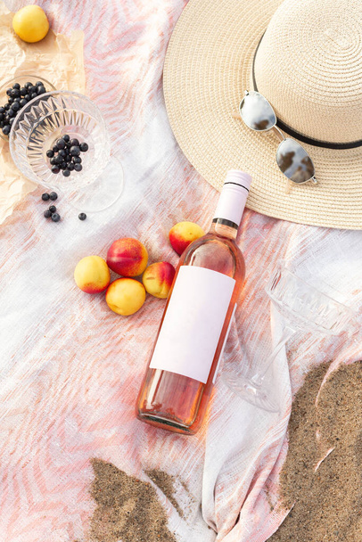 Summer beach picnic on the coast. Bottle of rose wine, fruits, summer accessories. Romantic party concept. Top view - 写真・画像