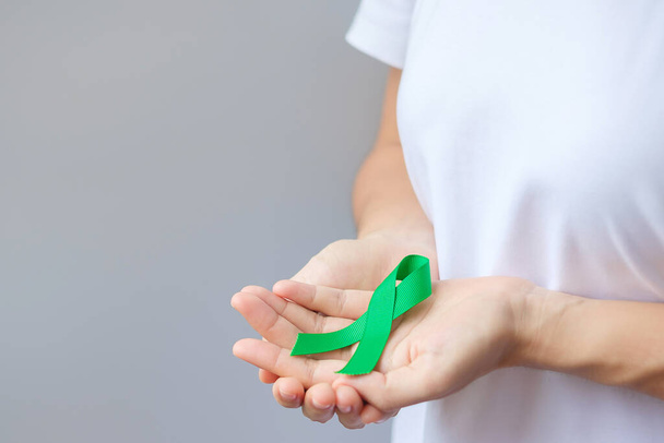 Mão segurando fita verde para fígado, vesícula biliar, ducto biliar, cervical, câncer de rim e linfoma mês de conscientização. Cuidados de saúde e conceito dia mundial do câncer - Foto, Imagem